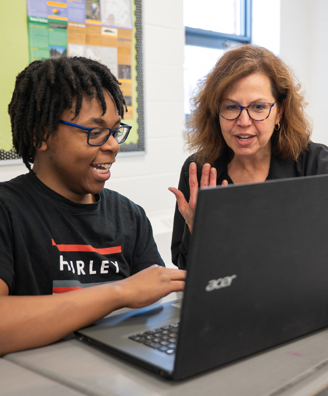 female teacher helping male student with his work on a laptop