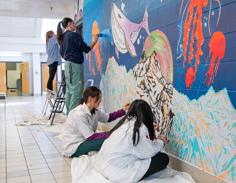 several students from art club working on large wall mural